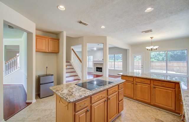 kitchen featuring pendant lighting, a kitchen island, a chandelier, stainless steel refrigerator, and black electric stovetop