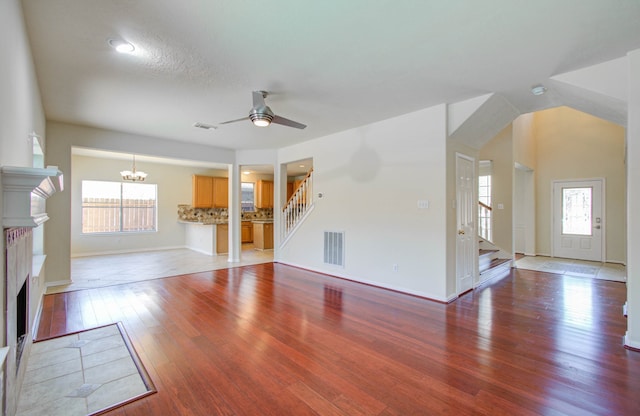 unfurnished living room featuring wood-type flooring, ceiling fan with notable chandelier, vaulted ceiling, and a wealth of natural light