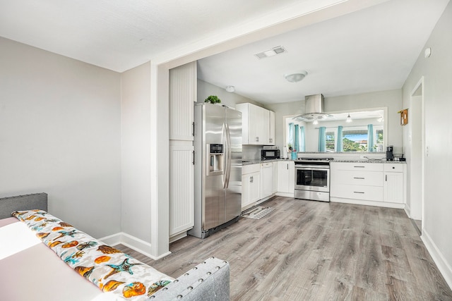 kitchen with appliances with stainless steel finishes, white cabinets, island range hood, light stone countertops, and light wood-type flooring