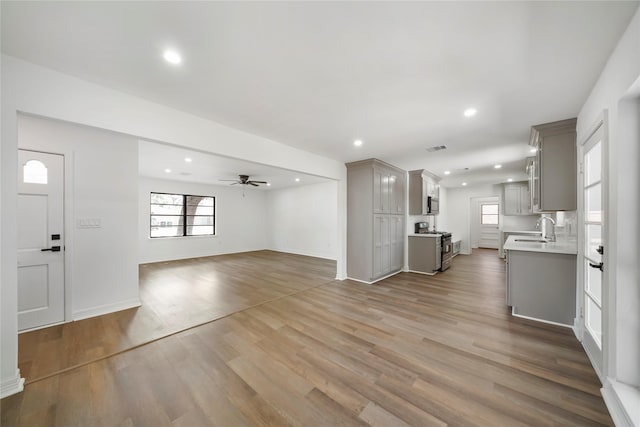 unfurnished living room with ceiling fan, a healthy amount of sunlight, wood-type flooring, and sink