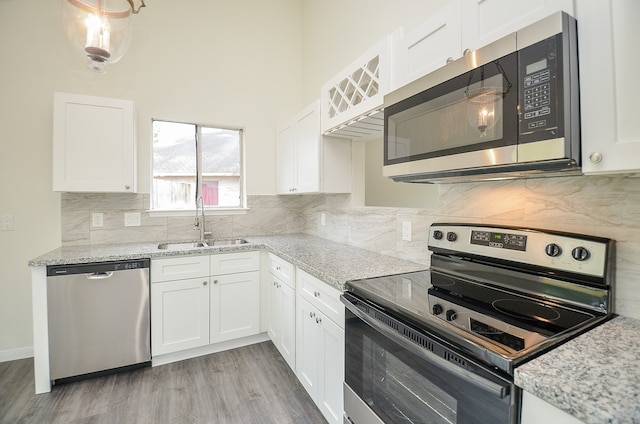 kitchen featuring white cabinetry, light stone counters, tasteful backsplash, stainless steel appliances, and light hardwood / wood-style flooring