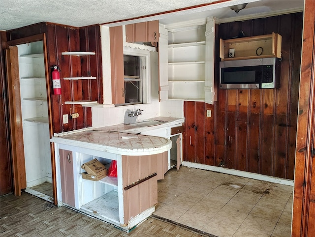 kitchen featuring a textured ceiling, wooden walls, backsplash, and sink