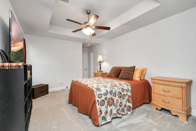 carpeted bedroom with a raised ceiling and ceiling fan