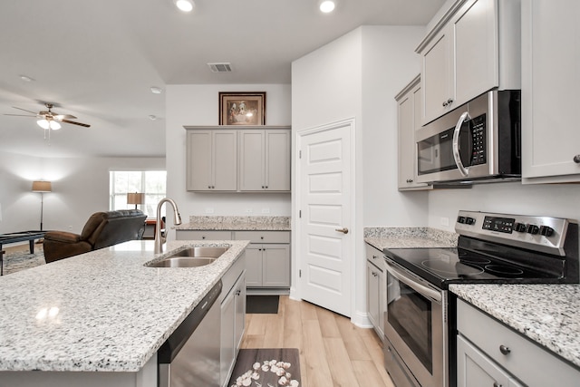 kitchen with sink, light hardwood / wood-style flooring, gray cabinets, an island with sink, and stainless steel appliances