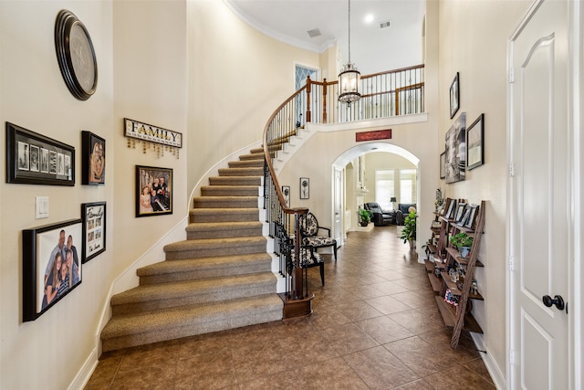 tiled entrance foyer with a notable chandelier, a towering ceiling, and ornamental molding