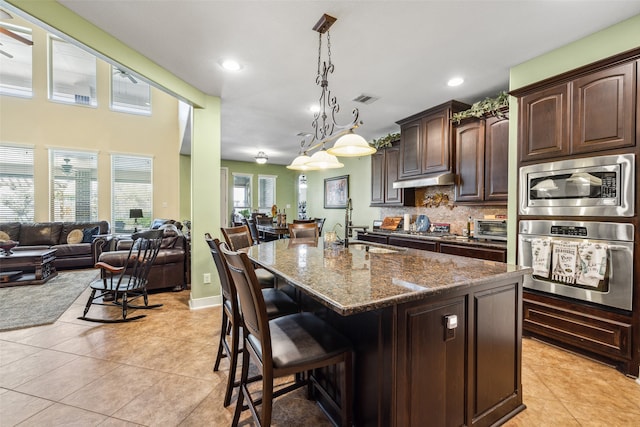 kitchen with a kitchen island with sink, hanging light fixtures, sink, appliances with stainless steel finishes, and dark brown cabinets