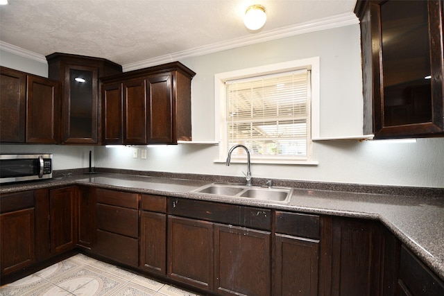 kitchen with a textured ceiling, dark brown cabinets, ornamental molding, and sink