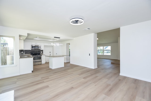 kitchen with white cabinets, pendant lighting, backsplash, stainless steel appliances, and light wood-type flooring