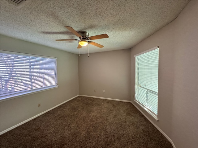 empty room with dark colored carpet, ceiling fan, a textured ceiling, and a wealth of natural light