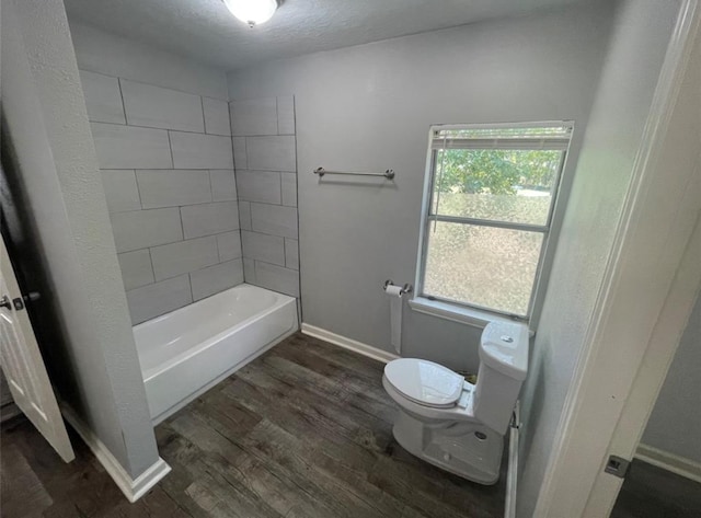 bathroom featuring wood-type flooring, a textured ceiling, tiled shower / bath, and toilet