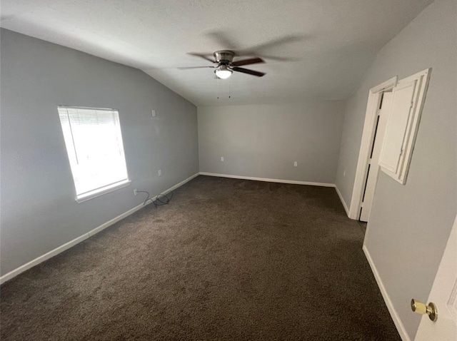 spare room featuring dark colored carpet, vaulted ceiling, and ceiling fan