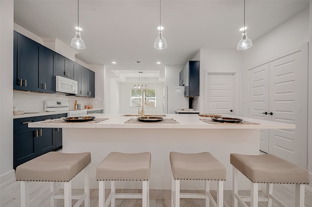 kitchen with white appliances, decorative light fixtures, and a breakfast bar area