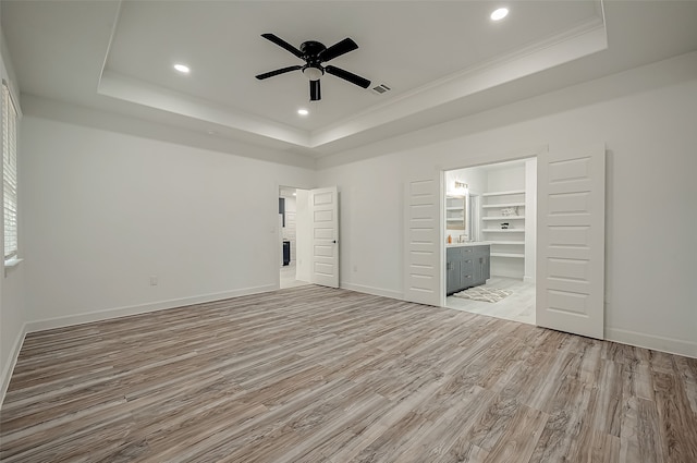 unfurnished bedroom featuring a tray ceiling, ensuite bathroom, light wood-type flooring, and ceiling fan