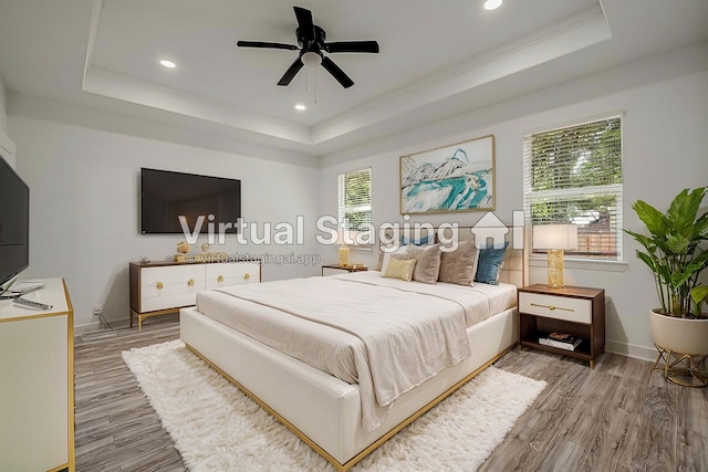 bedroom with a raised ceiling, wood-type flooring, multiple windows, and ceiling fan