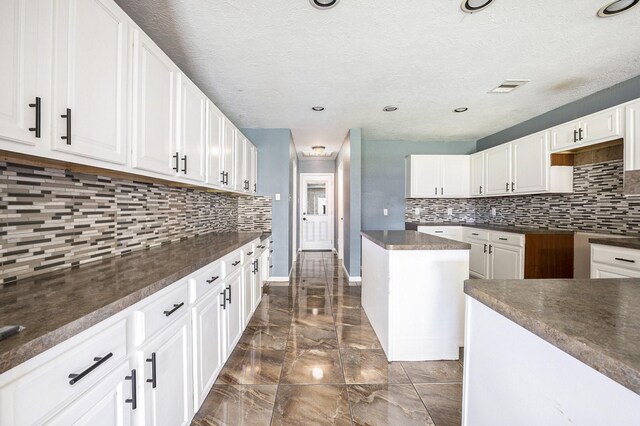 kitchen with white cabinets, a kitchen island, a textured ceiling, and decorative backsplash