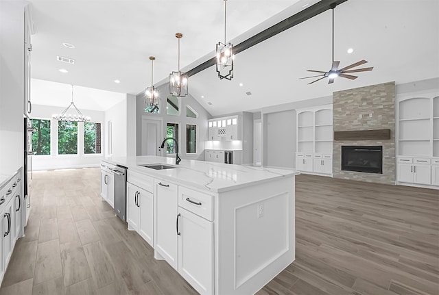 kitchen featuring an island with sink, a tile fireplace, pendant lighting, white cabinetry, and light stone counters