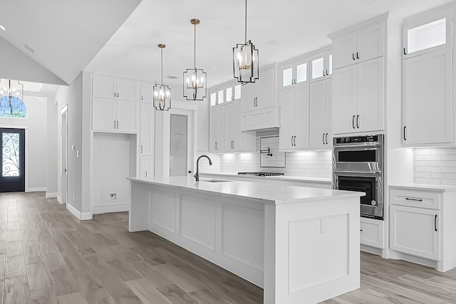 kitchen with appliances with stainless steel finishes, sink, pendant lighting, white cabinets, and a center island with sink