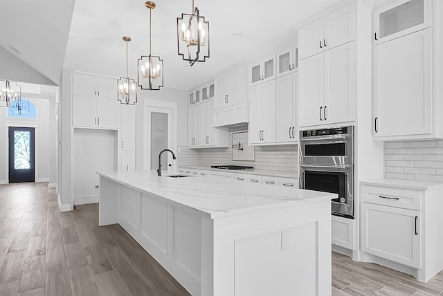 kitchen featuring light stone countertops, sink, backsplash, white cabinets, and a center island with sink