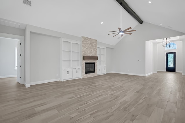 unfurnished living room featuring ceiling fan with notable chandelier, a fireplace, built in features, beam ceiling, and light hardwood / wood-style flooring