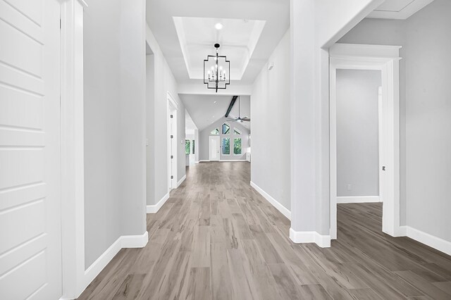 hall with a tray ceiling, light hardwood / wood-style flooring, and an inviting chandelier