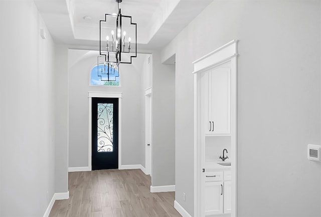 foyer featuring sink, a notable chandelier, a tray ceiling, and light hardwood / wood-style flooring