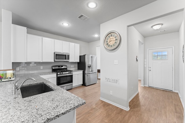 kitchen featuring appliances with stainless steel finishes, white cabinetry, light stone counters, and sink