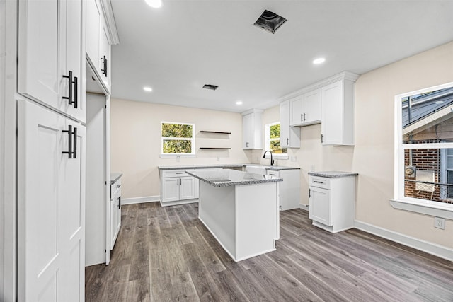 kitchen featuring white cabinetry, dark hardwood / wood-style floors, light stone countertops, and a kitchen island