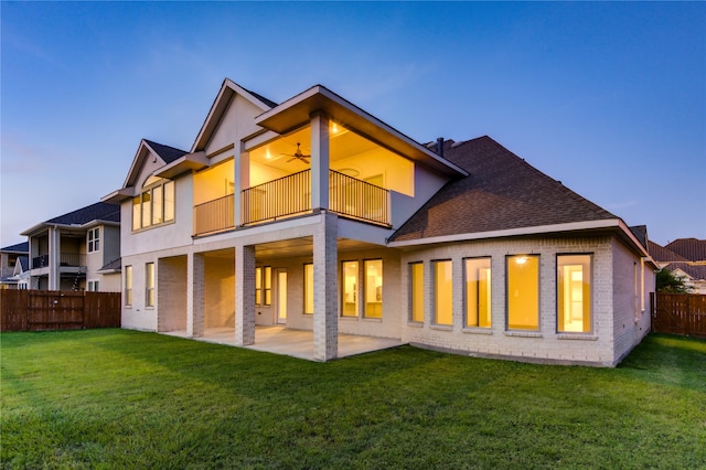 back house at dusk with a lawn, a balcony, and a patio