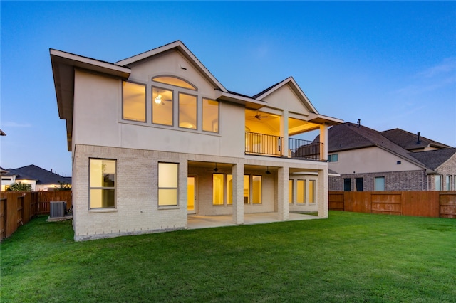 rear view of property featuring ceiling fan, a balcony, a yard, and a patio