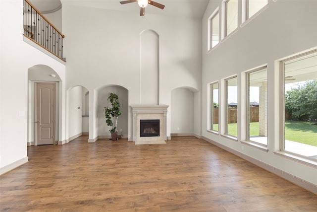 unfurnished living room featuring a towering ceiling, ceiling fan, hardwood / wood-style flooring, and a fireplace