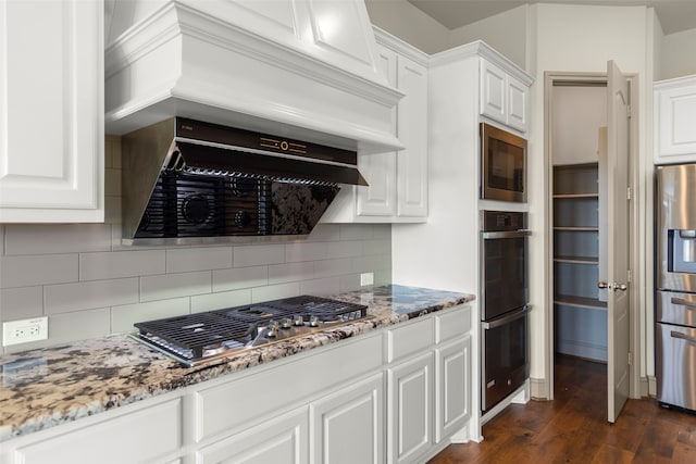 kitchen with dark wood-type flooring, white cabinets, appliances with stainless steel finishes, extractor fan, and stone countertops