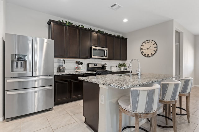 kitchen featuring sink, dark brown cabinets, light tile patterned floors, a center island with sink, and appliances with stainless steel finishes