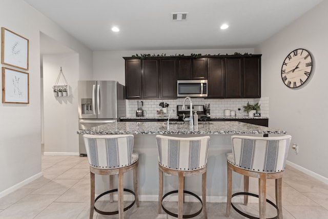 kitchen with appliances with stainless steel finishes, dark brown cabinetry, sink, light tile patterned floors, and an island with sink