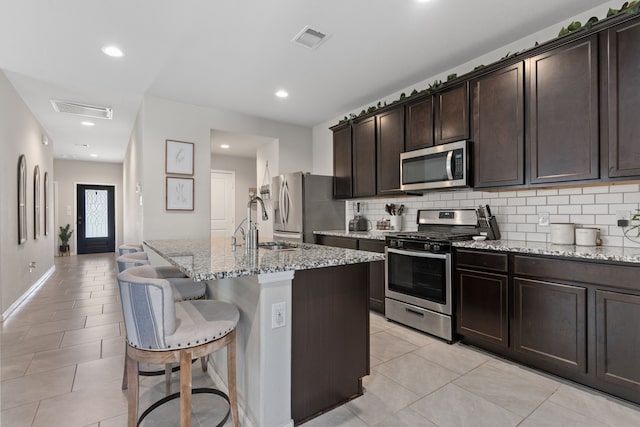 kitchen featuring light stone counters, light tile patterned floors, a kitchen island with sink, and appliances with stainless steel finishes