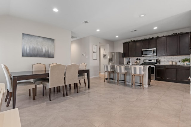 kitchen featuring appliances with stainless steel finishes, light stone counters, dark brown cabinets, a breakfast bar area, and an island with sink