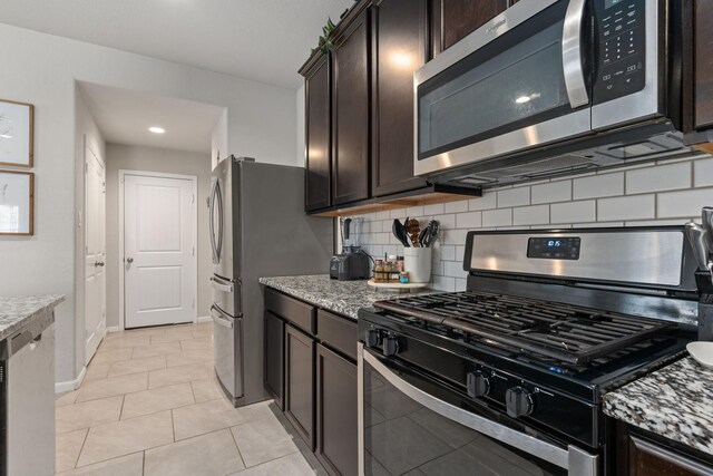 kitchen with backsplash, dark brown cabinets, light tile patterned flooring, light stone counters, and stainless steel appliances