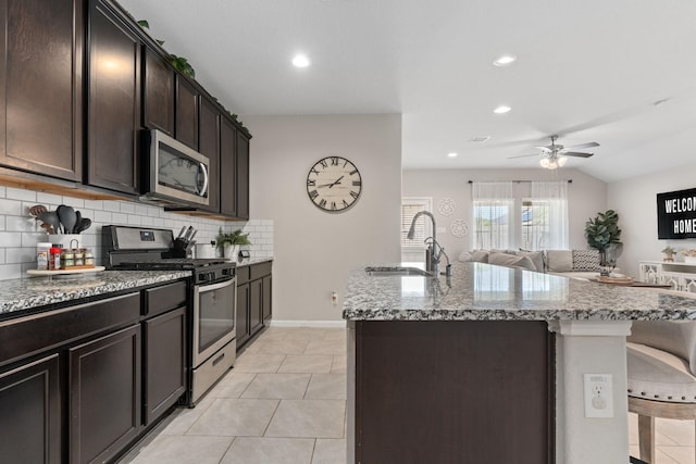 kitchen with a kitchen island with sink, sink, dark brown cabinets, light tile patterned flooring, and stainless steel appliances