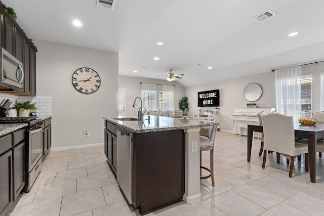 kitchen featuring light stone countertops, appliances with stainless steel finishes, ceiling fan, a kitchen island with sink, and sink