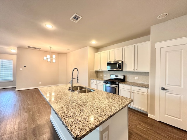 kitchen with light stone counters, white cabinets, stainless steel appliances, a kitchen island with sink, and sink