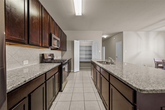 kitchen with dark brown cabinetry, stainless steel appliances, sink, light tile patterned floors, and a center island with sink