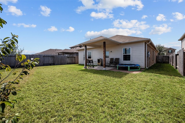 rear view of property with a lawn, a trampoline, and a patio