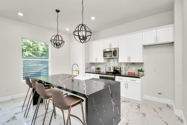 kitchen with white cabinets, stainless steel appliances, a center island with sink, and backsplash