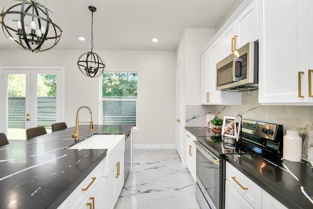 kitchen with pendant lighting, appliances with stainless steel finishes, white cabinets, decorative backsplash, and a chandelier