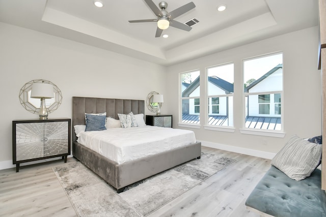 bedroom featuring light wood-type flooring, ceiling fan, and a tray ceiling