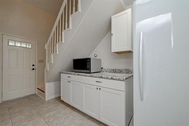 kitchen featuring white refrigerator, light tile patterned flooring, white cabinetry, light stone countertops, and vaulted ceiling