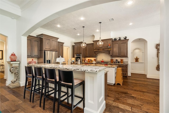 kitchen featuring dark wood-style floors, arched walkways, a center island with sink, visible vents, and appliances with stainless steel finishes