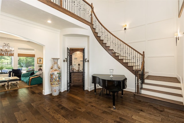 entrance foyer featuring a chandelier, a decorative wall, dark wood-type flooring, ornamental molding, and stairway