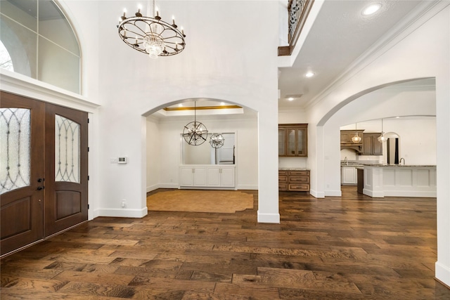 foyer entrance with arched walkways, an inviting chandelier, dark wood finished floors, and crown molding