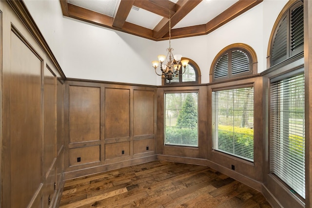 unfurnished dining area with coffered ceiling, dark wood-style flooring, beamed ceiling, an inviting chandelier, and a decorative wall