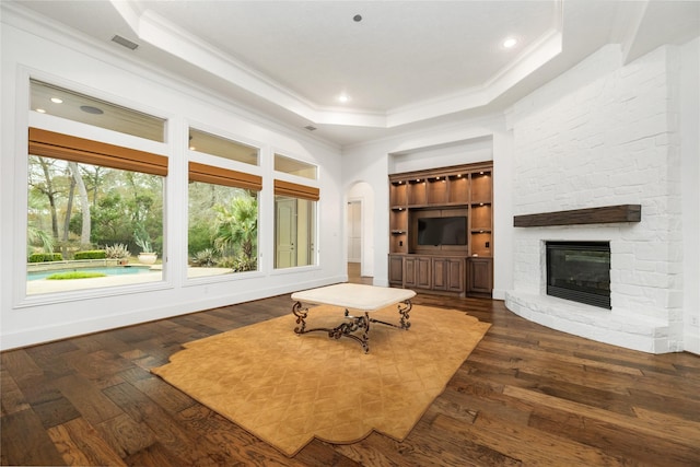 living room featuring a raised ceiling, ornamental molding, a stone fireplace, and dark hardwood / wood-style flooring